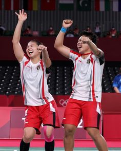 two young men standing next to each other holding their hands in the air while wearing red shorts