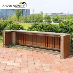 a wooden bench sitting on top of a brick floor next to bushes and trees in front of a building