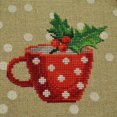 a cross stitch christmas mug with holly on the top and white polka dots around it