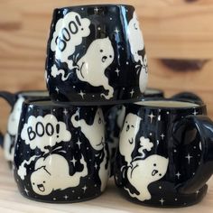 four black and white coffee mugs with ghost images on them, all stacked together