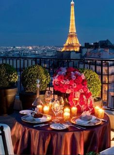 the table is set with candles, plates and flowers in front of the eiffel tower