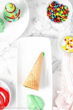 an ice cream cone on a white plate with candy and candies in bowls next to it