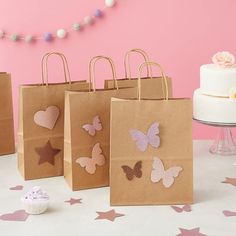 small brown paper bags with pink and purple butterflies on them sitting on a table next to a cupcake