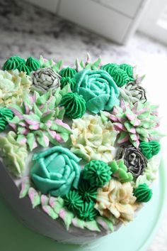 a cake decorated with green frosting and flowers on top of a table next to a window