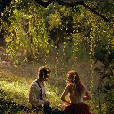 a man and woman sitting on the ground next to each other in front of trees