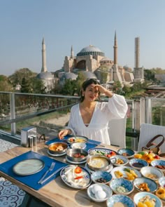 a woman sitting at a table with plates of food on it in front of a large building