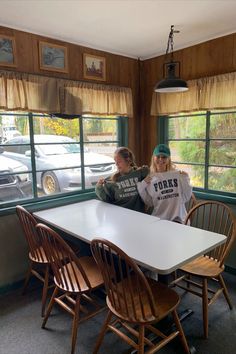 two people sitting at a table in a room with wooden chairs and large windows looking out onto the parking lot