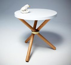 a small white table with wooden legs and a bird on it's top, against a gray background