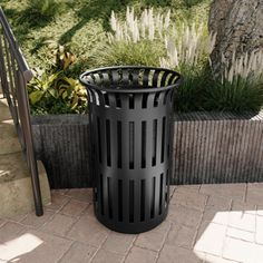 a black trash can sitting on top of a brick sidewalk next to a planter