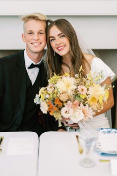 a bride and groom pose for a photo in front of a table with flowers on it