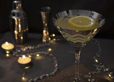 a martini glass with lemon on the rim and candles in the background, along with other glasses