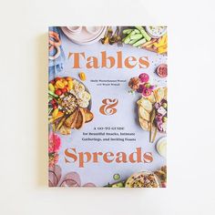 Against a white background is the cover of a cook book. The cover is the birds eye view of a gray table. Around the edges of the cover are trays of food such as vegetables, humus, crackers and flowers. In the middle is rose gold text that reads ‘tables & spreads.’ Platter Board, Family Brunch, Dinner For One, Dutch Baby, Farm To Table, Grazing Tables, Easy Entertaining, Feeding A Crowd, Lettuce Wraps