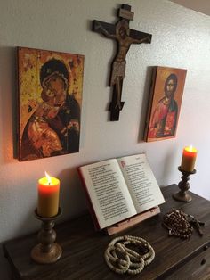 an open book sitting on top of a wooden table next to a cross and candles