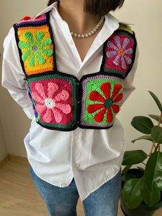 a woman wearing a white shirt and colorful crocheted vest