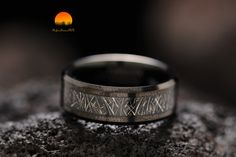 a wedding band with an etched design on it sitting on top of a rock in front of the sun