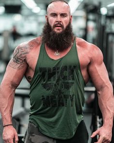 a man with a long beard standing in front of a barbell rack and wearing a green tank top