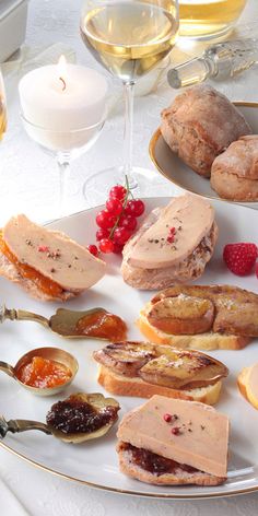 a plate with bread, fruit and jams on it next to some wine glasses