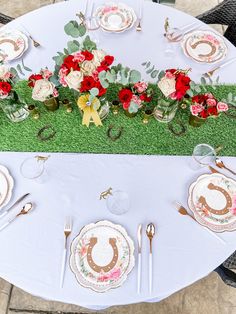 the table is set with plates, silverware and red flowers on top of green grass