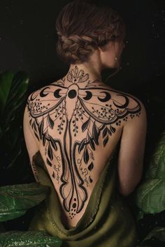 the back of a woman's body with tattoos on her neck and shoulder, in front of green leaves