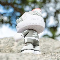 a close up of a toy shoe on top of a rock with trees in the background