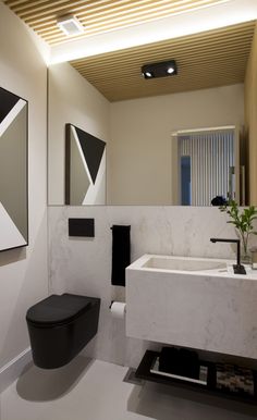 a bathroom with a black toilet sitting next to a white sink and a painting on the wall