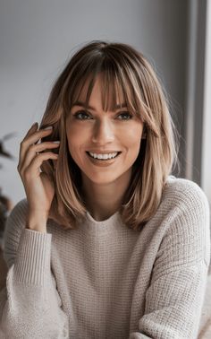 For a warm, cozy style, this mid-length haircut with bangs is perfect. The soft blonde hair with subtle waves adds a gentle touch, making it ideal for a round face. The light beige sweater enhances the casual, comfortable vibe, making this haircut perfect for clients looking for a low-maintenance yet chic style for everyday wear. Shoulder Length Hair With Layers And Curtain Bangs Straight Hair, Curtain Wispy Bangs Short Hair, Egyptian Haircut, Fine Hair Round Face Hairstyles, Bob Cut With Bangs Round Face, Straight Haircut With Bangs, Mid Length Fine Hair, Mid Blonde Hair, Shoulder Length Hair With Fringe