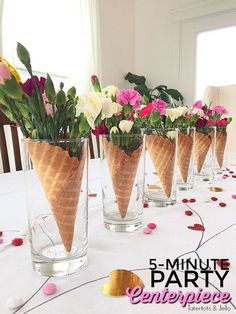 four ice cream cones with flowers in them on a white tableclothed table cloth