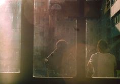 two people standing in front of a window with the sun shining on them and buildings behind them