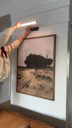 a woman holding a light above a painting on the wall