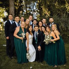 a group of people standing next to each other in front of trees and grass with one woman wearing a green dress