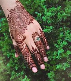 a henna tattoo on someone's hand in front of some green plants and bushes