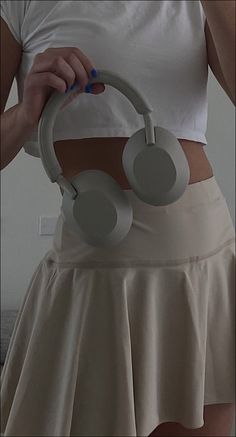 a woman in a white shirt and tan skirt holding a pair of headphones on her hip