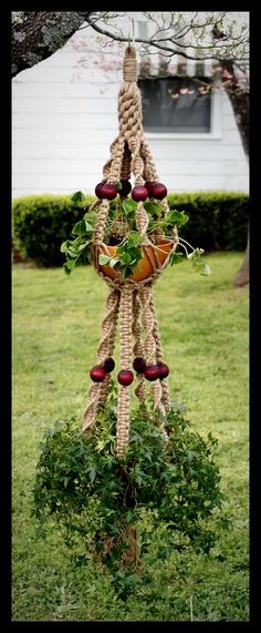 a hanging planter made out of rope and fruit on top of some grass in front of a house