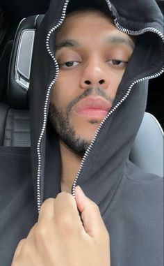 a man wearing a hoodie in the back seat of a car with his hand under his chin