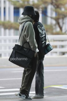 two people standing next to each other on the street, one carrying a black bag