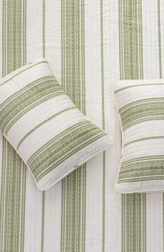 two green and white striped pillows sitting on top of a bed next to each other