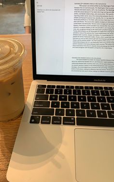 an open laptop computer sitting on top of a wooden table next to a cup of coffee