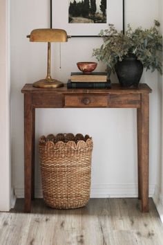 a wooden table topped with a basket next to a lamp and painting on the wall