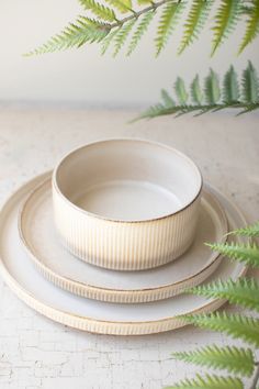 a set of three white dishes sitting on top of a table next to a green plant