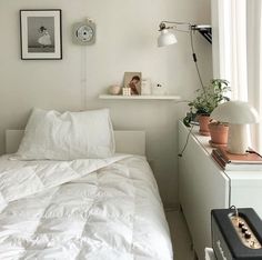 a white bed sitting under a window next to a lamp and pictures on the wall