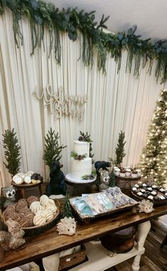 a table topped with lots of desserts next to a white christmas tree and curtain