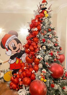 a christmas tree with mickey mouse decorations and red balls on the top is surrounded by other ornaments