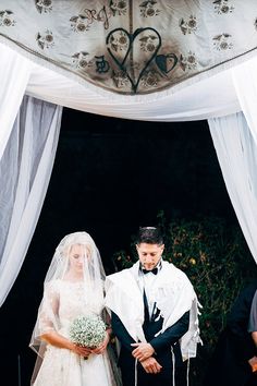 a bride and groom are standing under a wedding chute with white draping