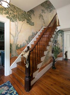 a staircase in a house painted with trees on the wall and below it is a tree mural