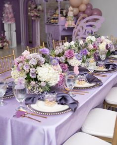 a long table with purple and white flowers on it is set for an event or party