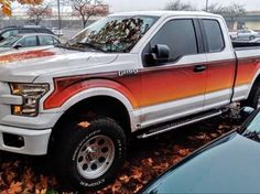 an orange and white truck parked in a parking lot next to other cars with leaves on the ground