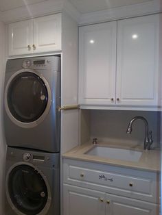 a washer and dryer in a white laundry room with cabinets on either side