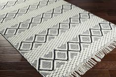 a white and black rug with fringes on top of wood flooring in a room