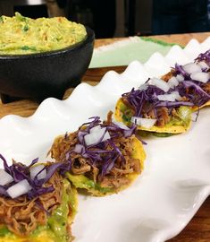 three tacos on a white plate next to a bowl of guacamole