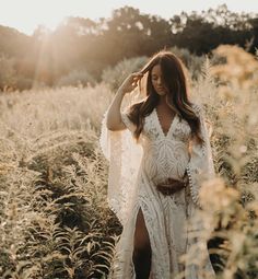 a pregnant woman in a white dress walking through tall grass